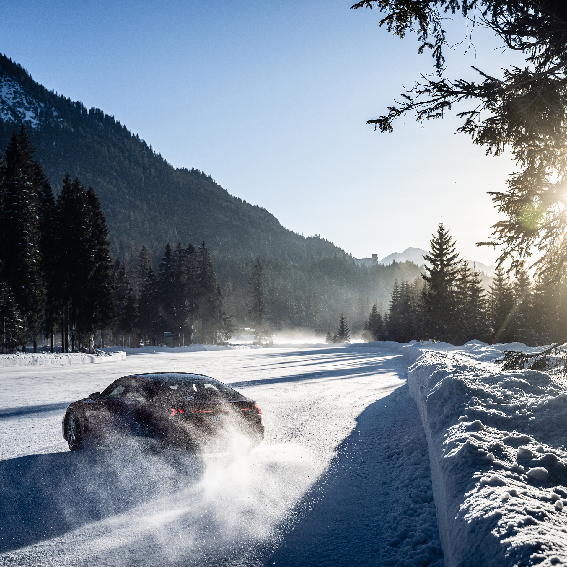 Schwarzer Audi RS 5 Sportback driftet im Schnee bei Sonnenschein und blauem Himmel. Im Hintergrund sind Bäume und Berge zu sehen.