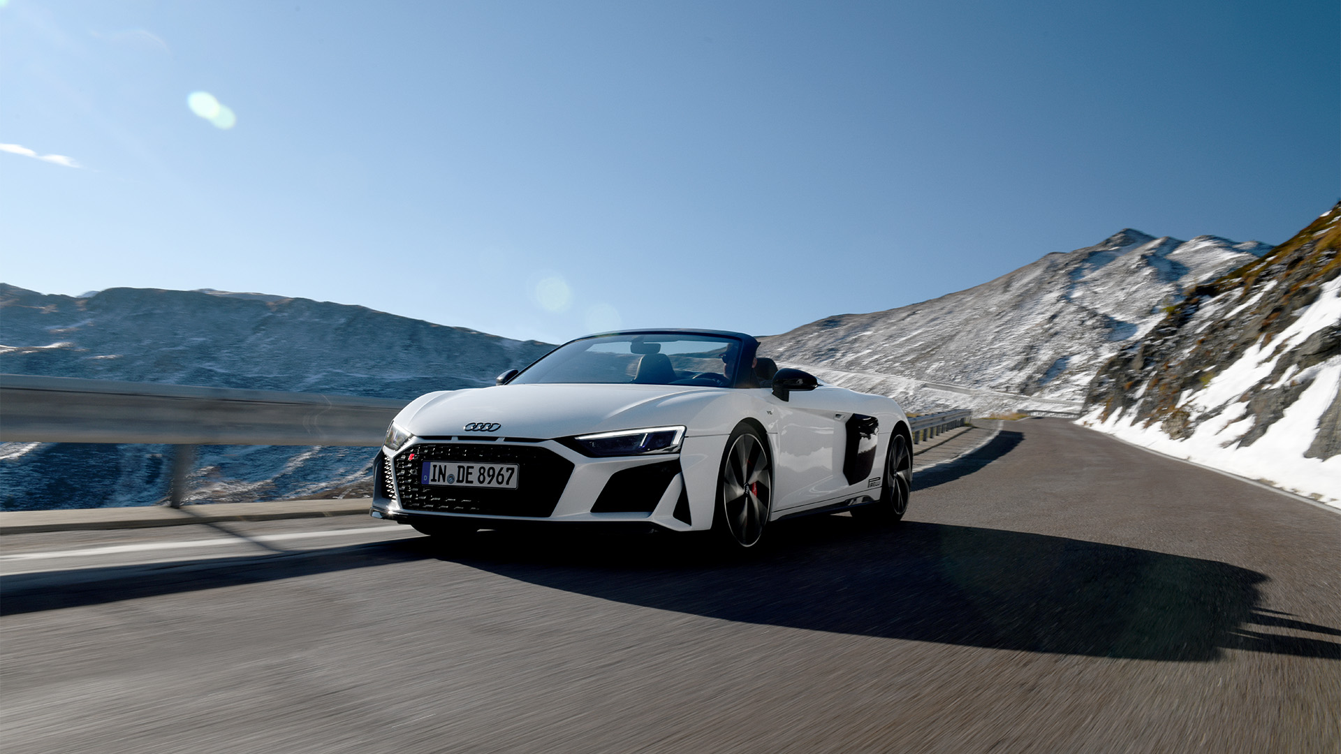 White Audi R8 Spyder V10 performance quattro (front view) driving on a road in the mountains under a blue sky