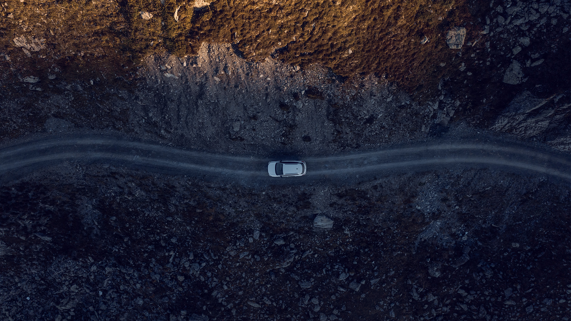 Ein Drohnenbild von oben zeigt ein weißes Auto auf einer Straße in den Bergen.