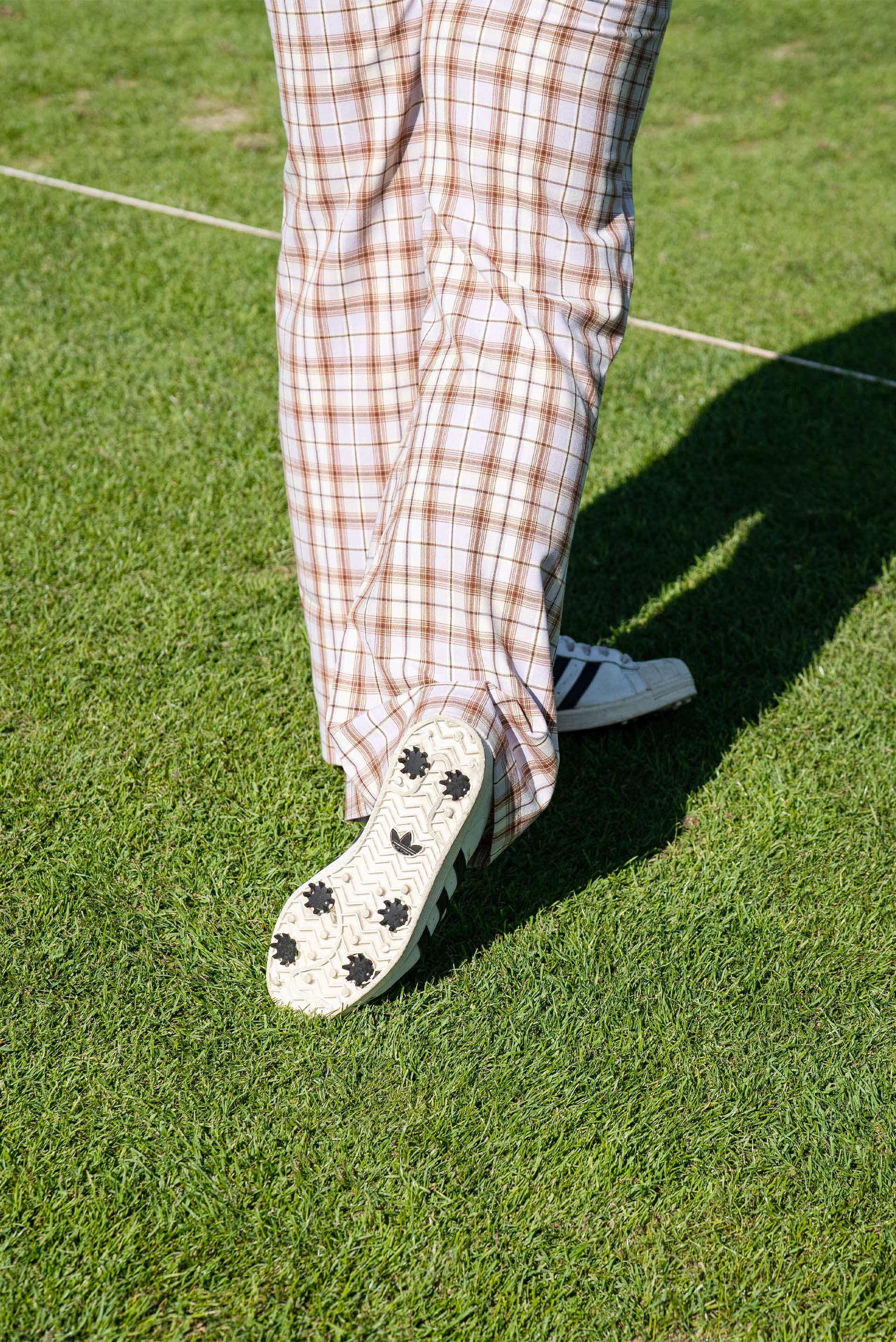 Detailaufnahme der karierten Golfhose und der Sneaker, die Mullins auf dem Golfplatz trägt. 