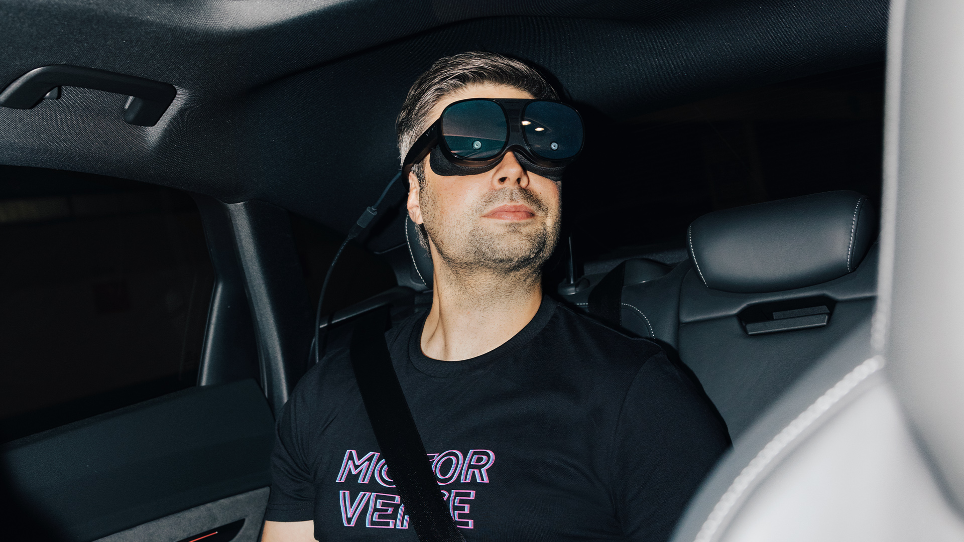 Nils Wollny sitzt auf dem Rücksitz eines Audi und trägt eine VR-Brille.